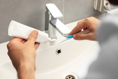 Photo of Man applying toothpaste on brush near sink in bathroom, closeup