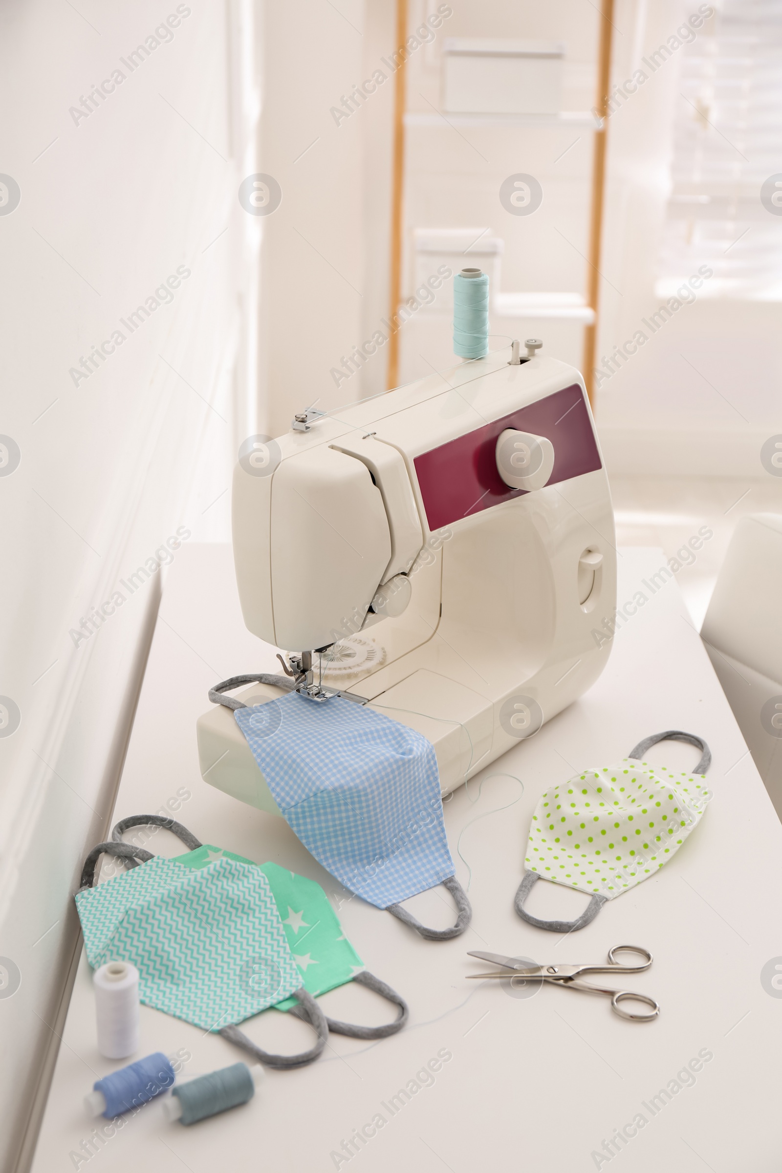Photo of Sewing machine with cloth mask on table indoors