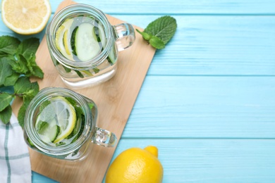 Photo of Refreshing water with cucumber, lemon and mint on light blue wooden table, flat lay. Space for text