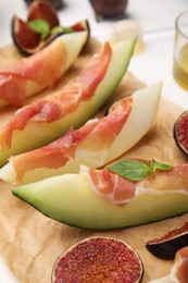 Photo of Tasty melon, jamon and figs served on parchment, closeup