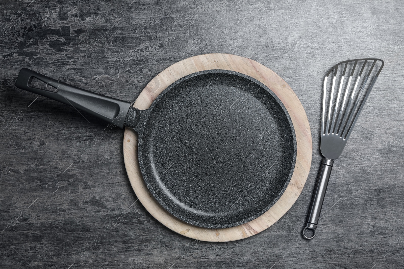 Photo of Cooking pan and slotted turner on grey table, flat lay. Kitchen utensils