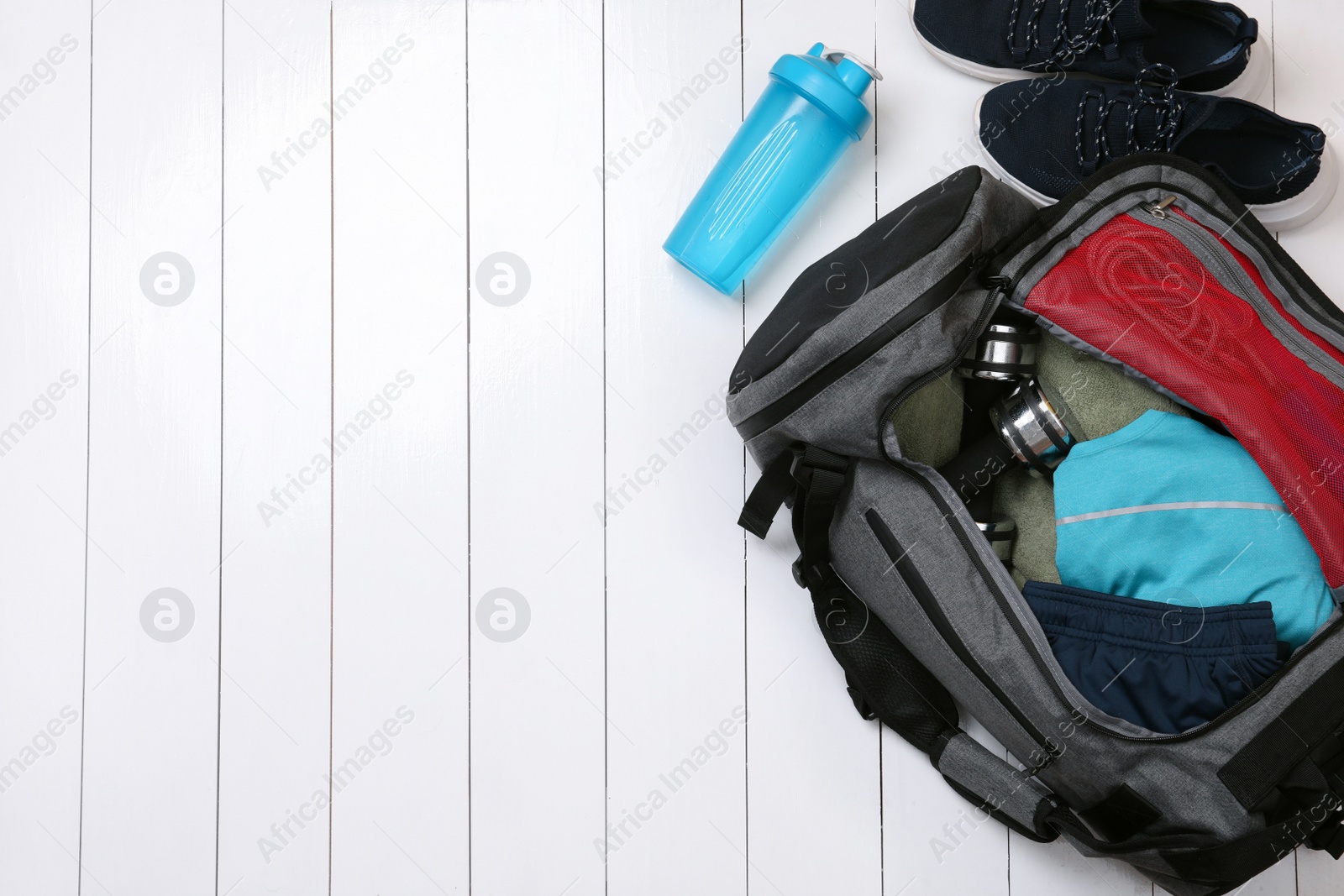 Photo of Gym bag and sports equipment on white wooden background, flat lay. Space for text