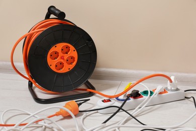 Photo of Extension cord reel plugged into socket on white floor indoors, space for text. Electrician's equipment