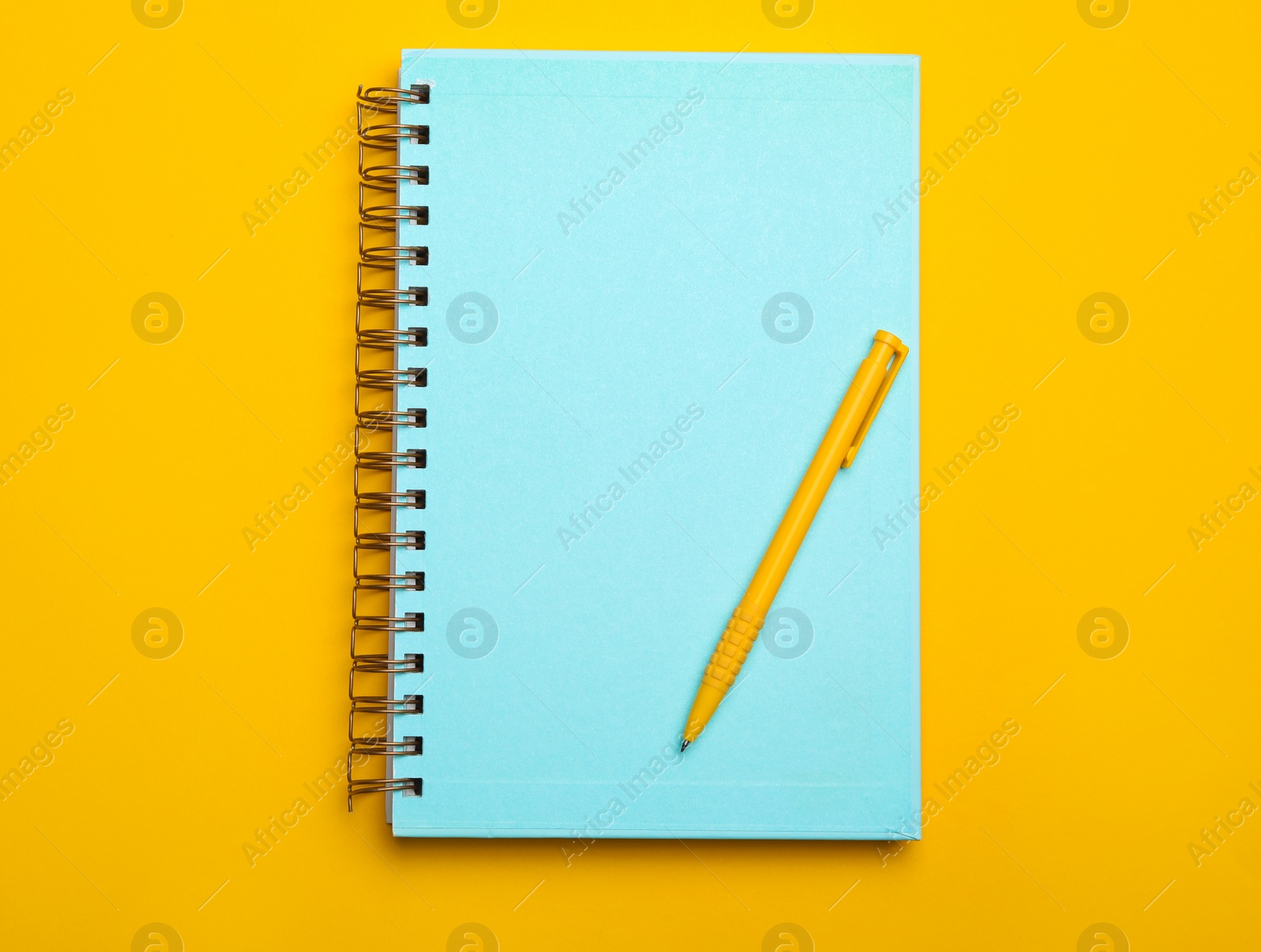 Photo of Light blue notebook and pen on yellow background, top view