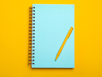 Photo of Light blue notebook and pen on yellow background, top view