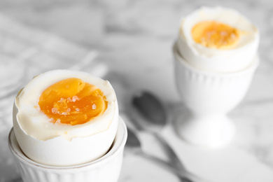 Photo of Tasty medium boiled egg in ceramic holder on white table, closeup