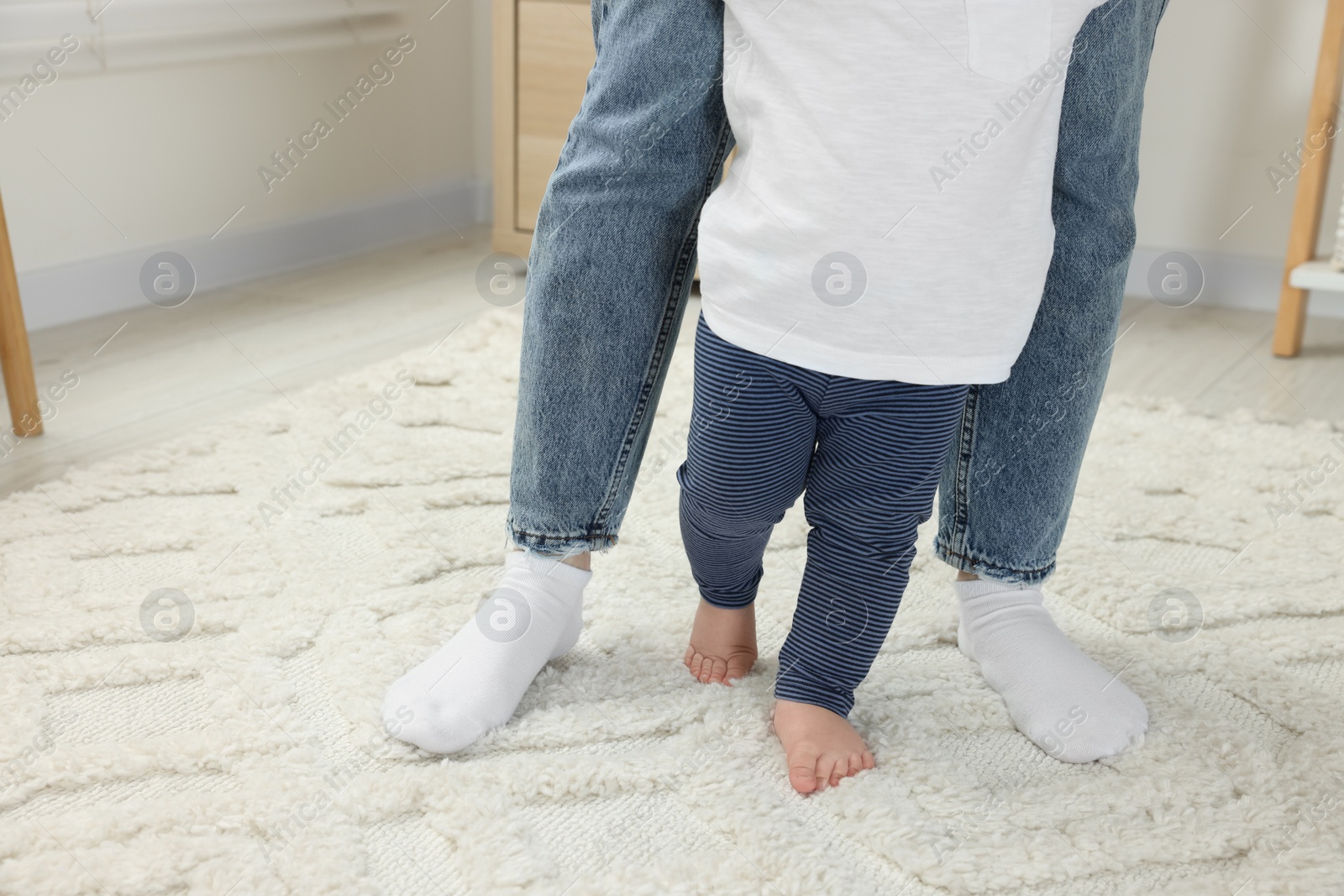 Photo of Mother supporting her son while he learning to walk on carpet indoors, closeup. Space for text