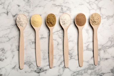 Spoons with different types of flour on marble background, top view