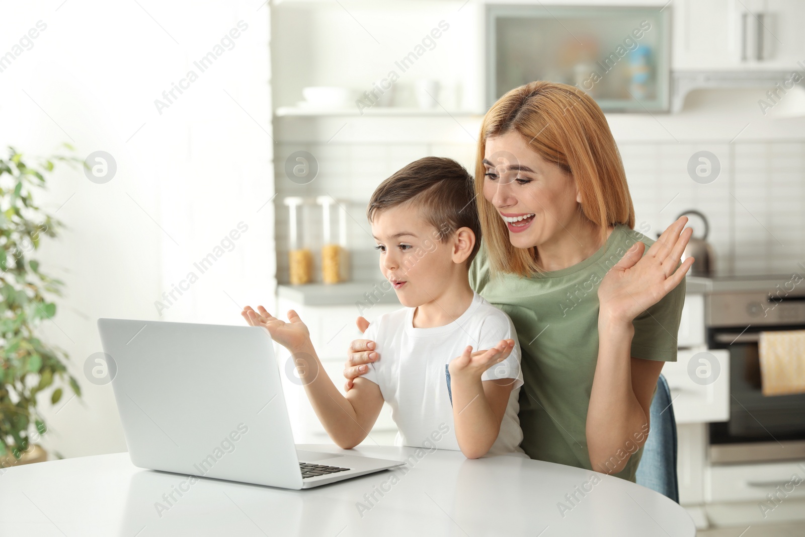 Photo of Mother and her son using video chat on laptop at table in kitchen