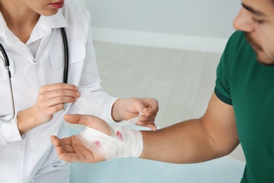 Photo of Female doctor applying bandage on young man's hand in clinic, closeup. First aid