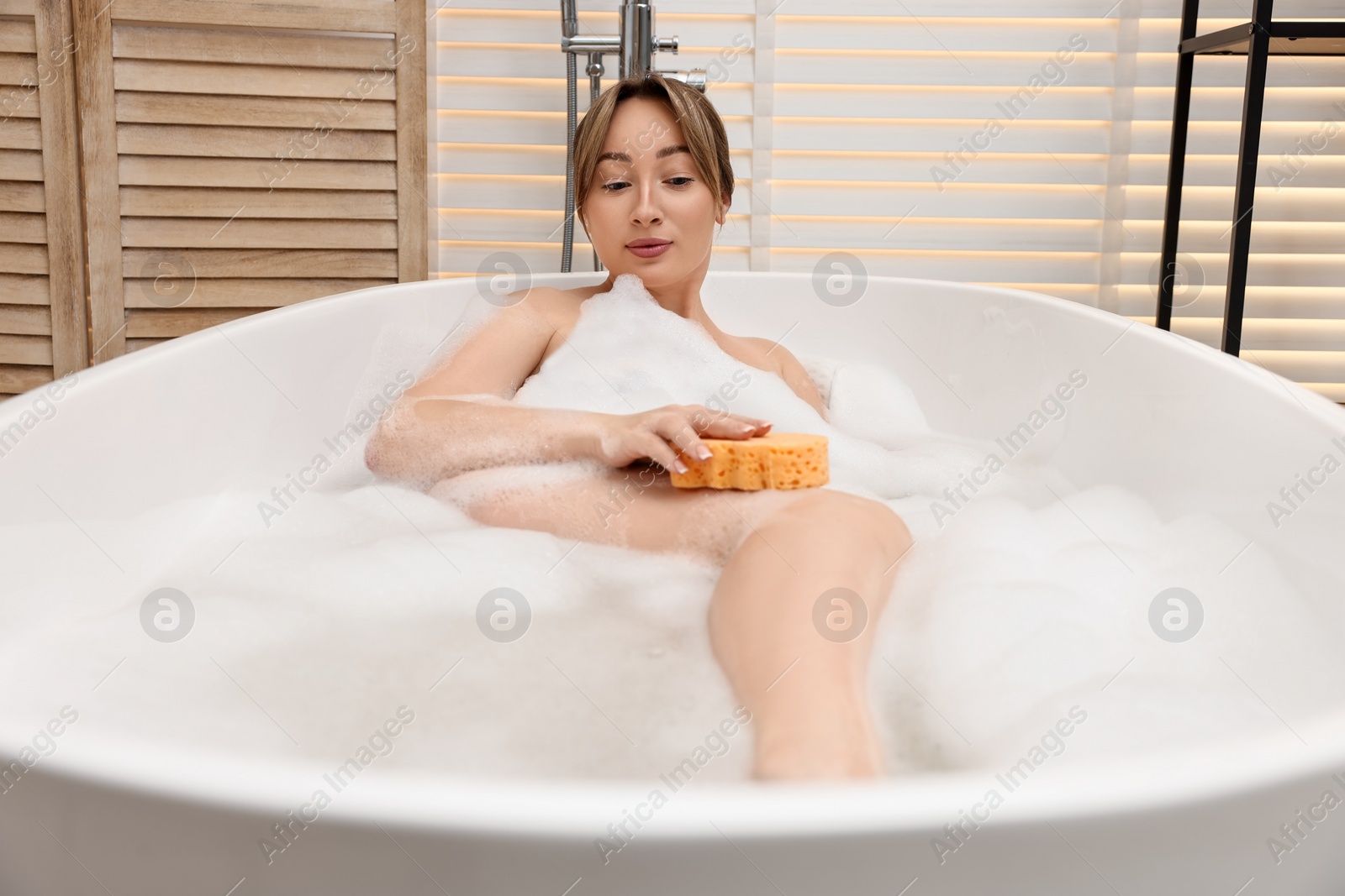 Photo of Beautiful woman taking bath with foam in tub indoors