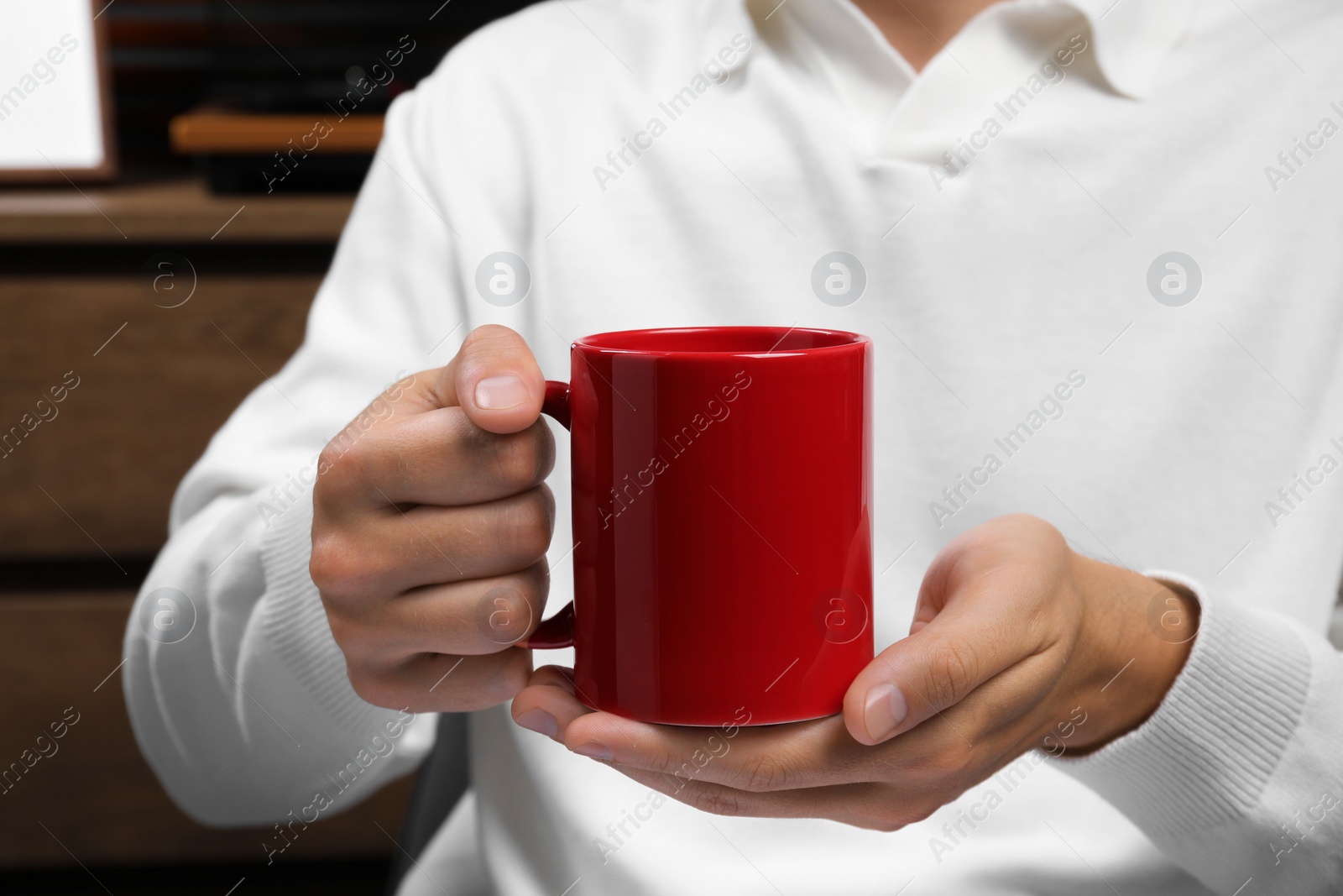 Photo of Man holding red mug indoors, closeup. Mockup for design