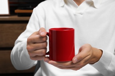 Photo of Man holding red mug indoors, closeup. Mockup for design