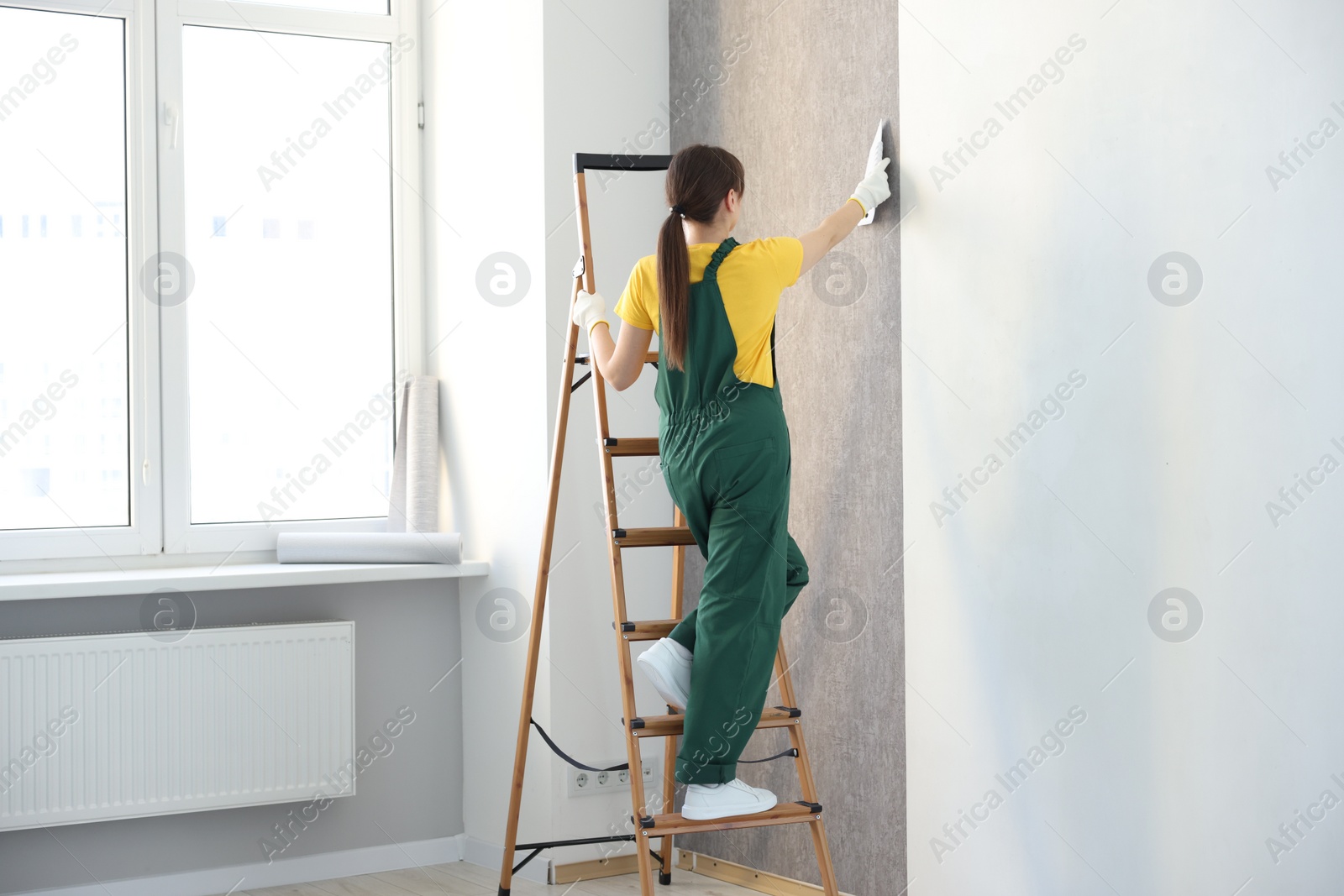 Photo of Woman smoothing stylish gray wallpaper in room