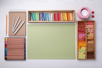 Photo of Layout with blank paper, soft pastels and other drawing supplies on white wooden table at artist's workplace, top view. Space for design