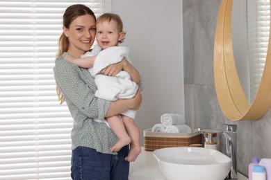 Mother holding cute little baby wrapped with towel indoors after bath, space for text