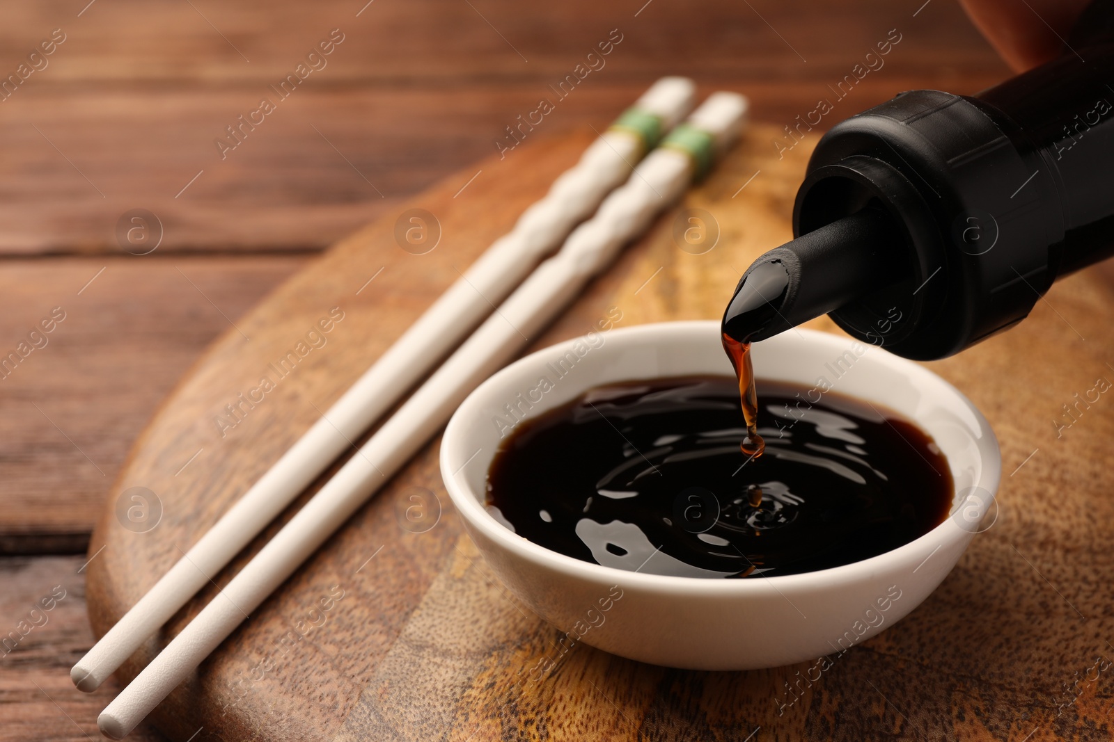 Photo of Pouring soy sauce from bottle into bowl on wooden board, closeup