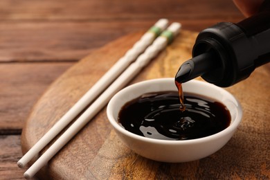 Pouring soy sauce from bottle into bowl on wooden board, closeup