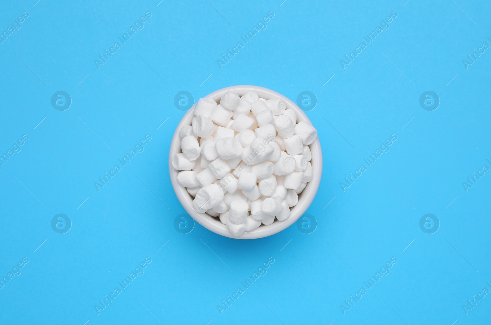 Photo of Bowl of sweet marshmallows on light blue background, top view