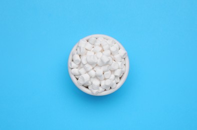 Bowl of sweet marshmallows on light blue background, top view