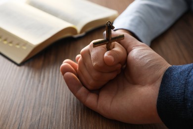 Photo of Boy and his godparent holding cross at wooden table, closeup