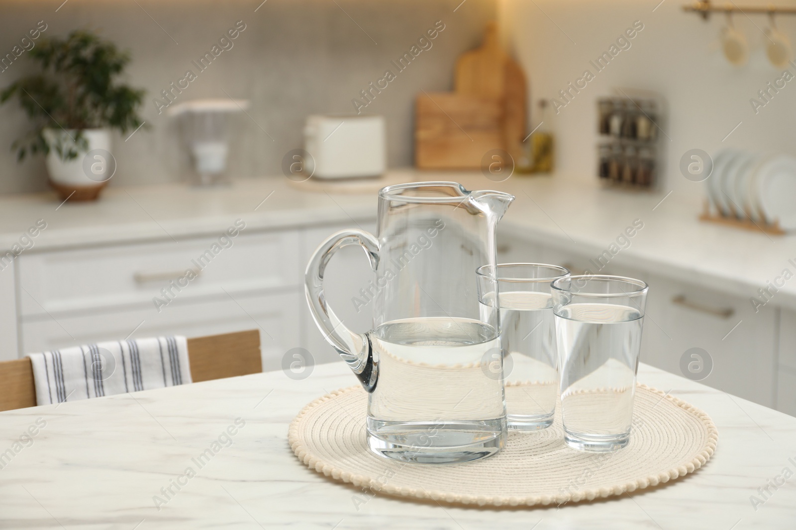 Photo of Jug and glasses with clear water on white table in kitchen, space for text