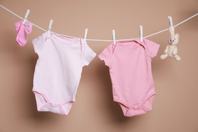 Photo of Cute small baby clothes and toy hanging on washing line against brown background