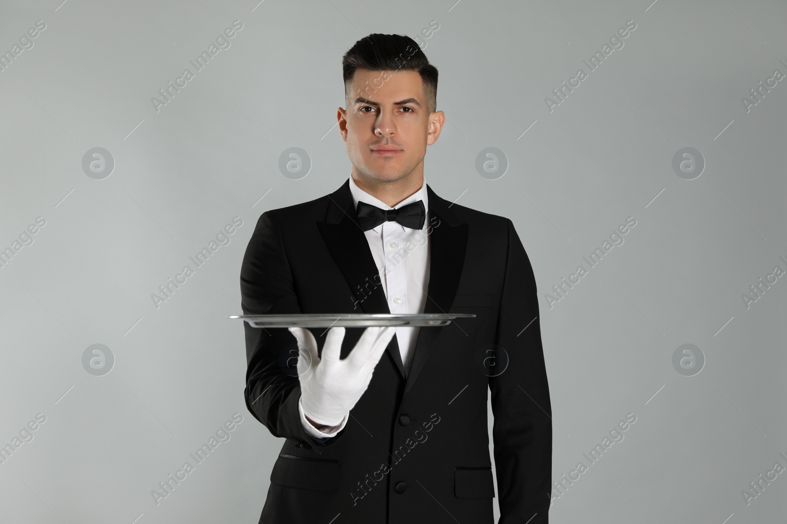 Photo of Handsome butler with tray on light grey background