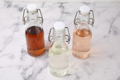 Photo of Different types of vinegar in bottles on light marble table, closeup