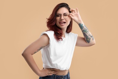 Photo of Beautiful tattooed woman showing her tongue on beige background