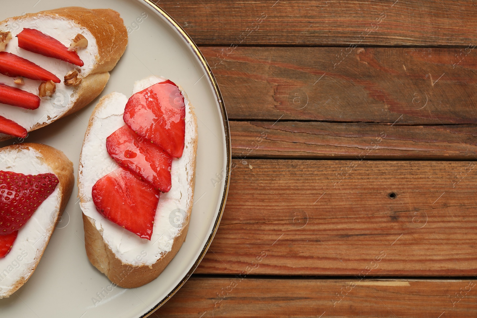 Photo of Delicious bruschettas with ricotta cheese and strawberries on wooden table, top view. Space for text