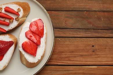 Delicious bruschettas with ricotta cheese and strawberries on wooden table, top view. Space for text