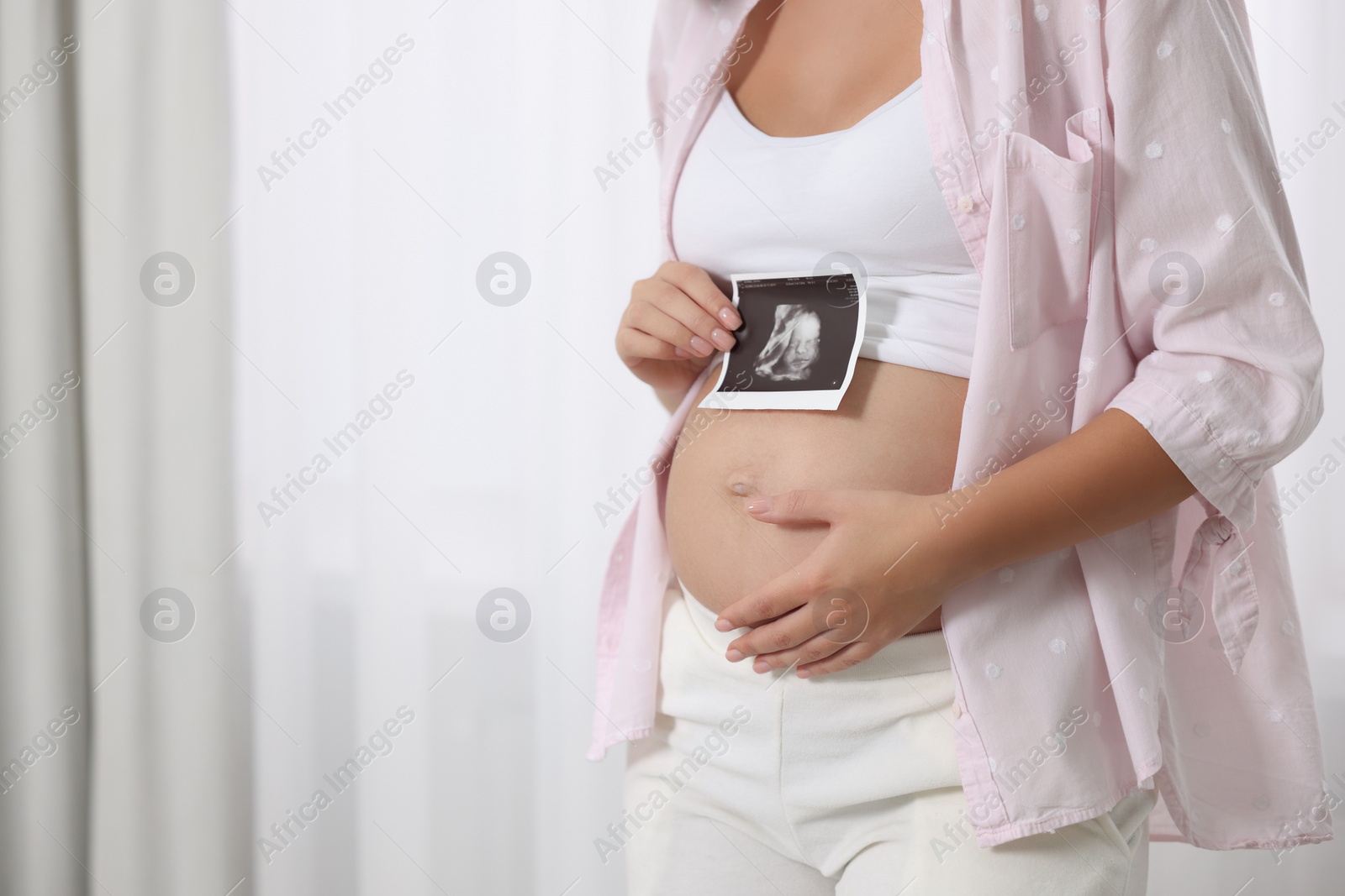 Photo of Pregnant woman with ultrasound picture of baby near window indoors, closeup. Space for text