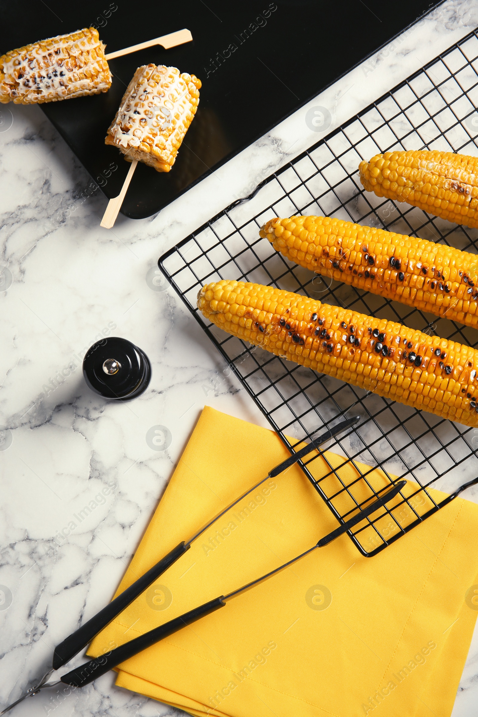 Photo of Cooling rack with grilled corn cobs on marble background, top view