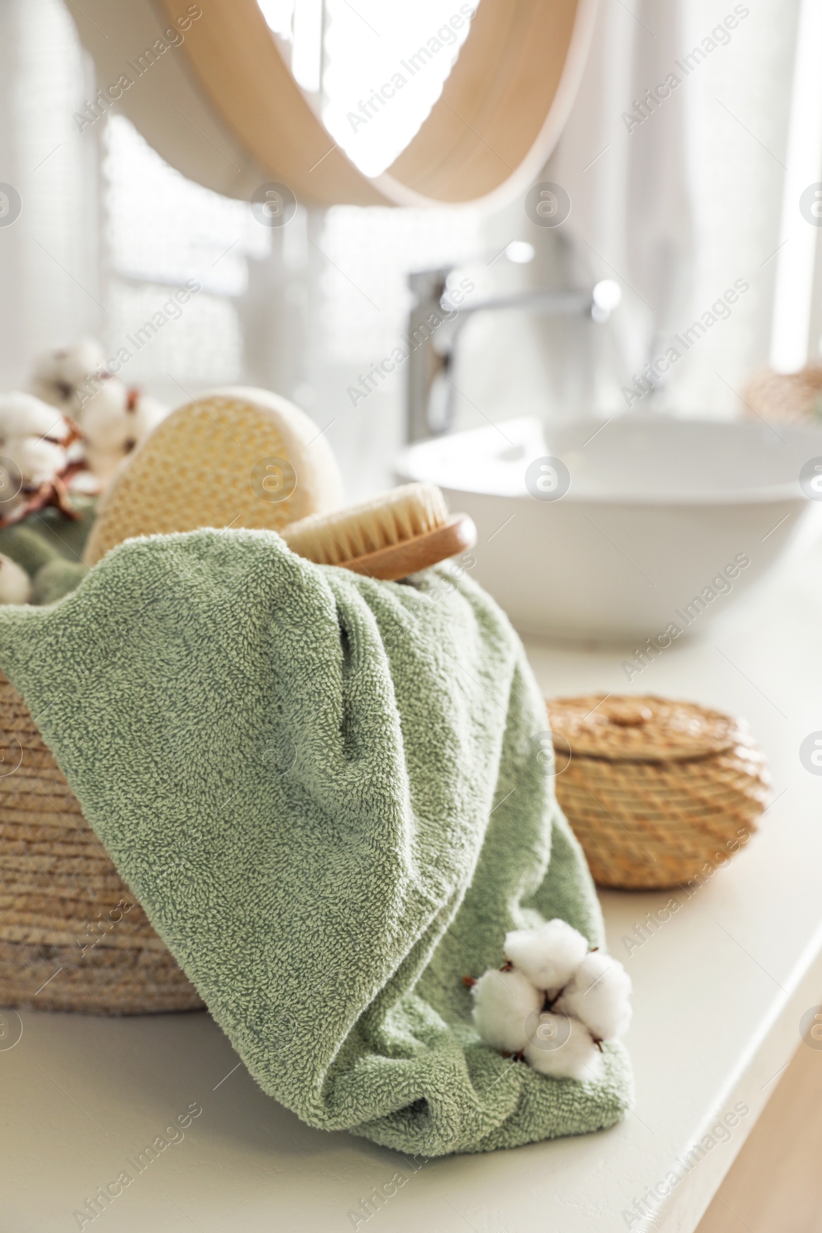 Photo of Wicker basket with clean towel, massage brush and cotton flowers on countertop in bathroom