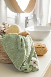 Photo of Wicker basket with clean towel, massage brush and cotton flowers on countertop in bathroom