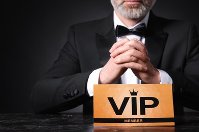 Man sitting at table with VIP sign on black background, closeup