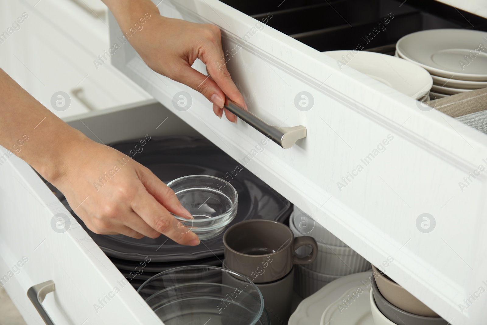 Photo of Woman taking glass bowl from open drawer of kitchen cabinet, closeup