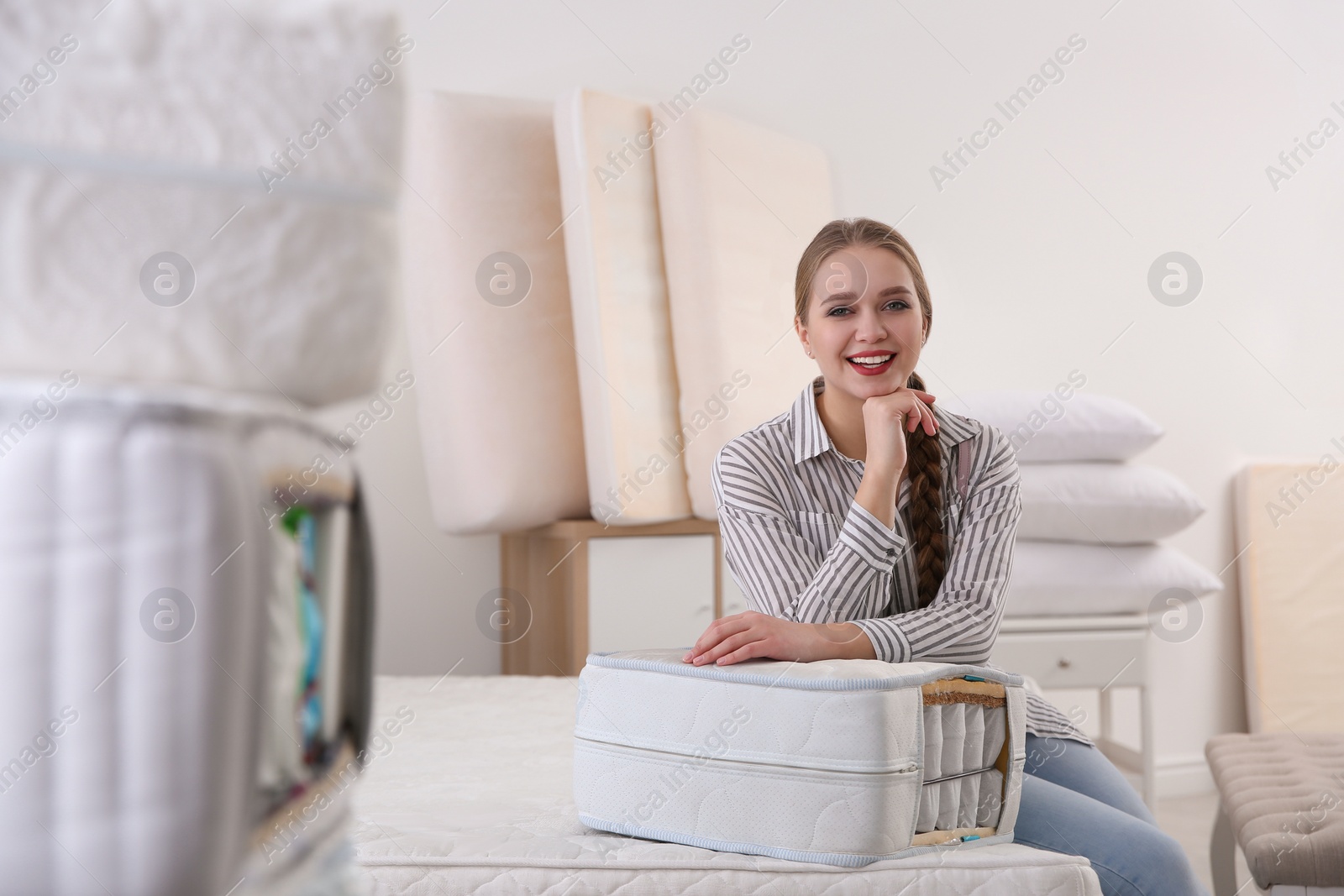 Photo of Young woman with section of mattress in furniture store. Space for text