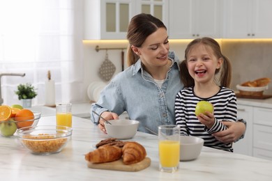 Photo of Mother and her cute little daughter having breakfast at table in kitchen