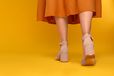 Woman wearing stylish shoes on yellow background, closeup. Space for text