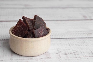 Photo of Delicious beef jerky in bowl on white wooden table, space for text