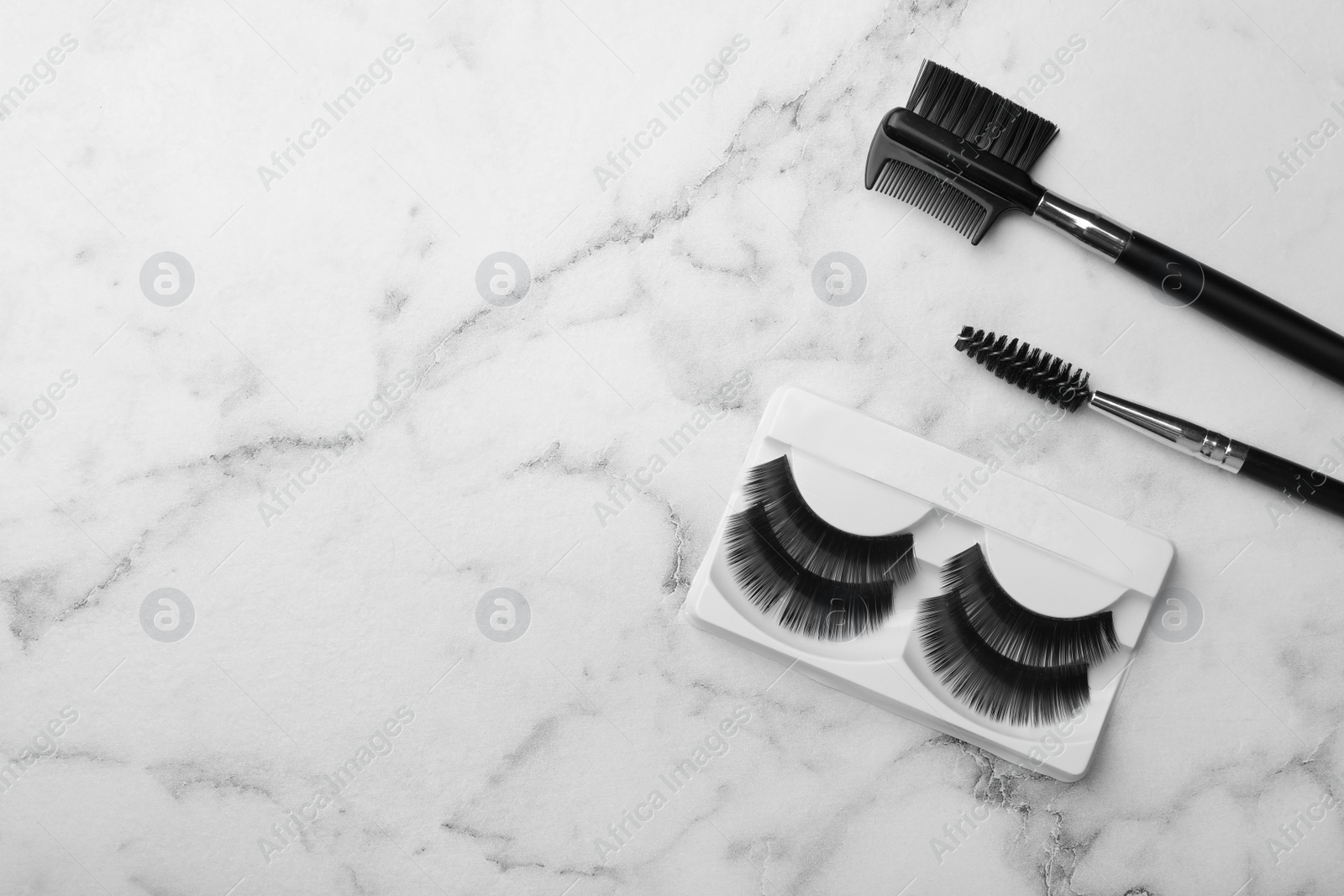 Photo of Artificial eyelashes and accessories on marble background, top view with space for text