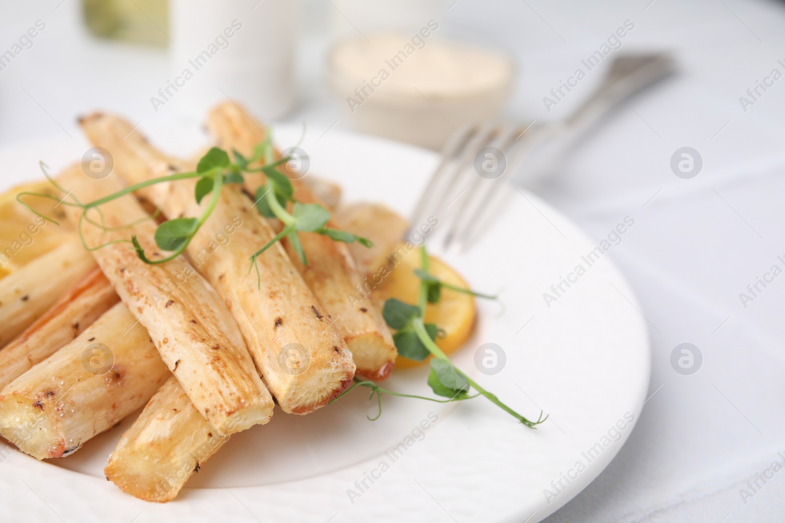 Photo of Plate with baked salsify roots and lemon on white table, closeup