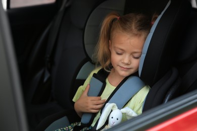 Photo of Cute little girl sleeping in child safety seat inside car
