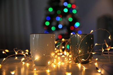 Photo of Cups, fairy lights and blurred Christmas tree on background