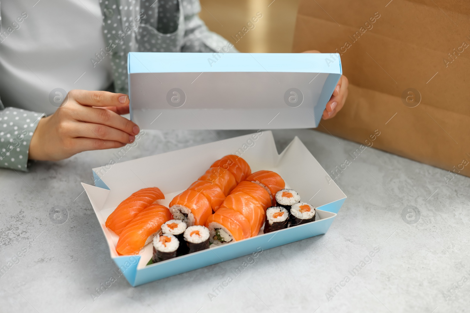 Photo of Woman unpacking her order from sushi restaurant at table in kitchen, closeup