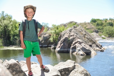 Photo of Little boy on rock near river. Summer camp
