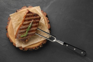 Photo of Delicious grilled beef steak and rosemary on dark gray table, top view