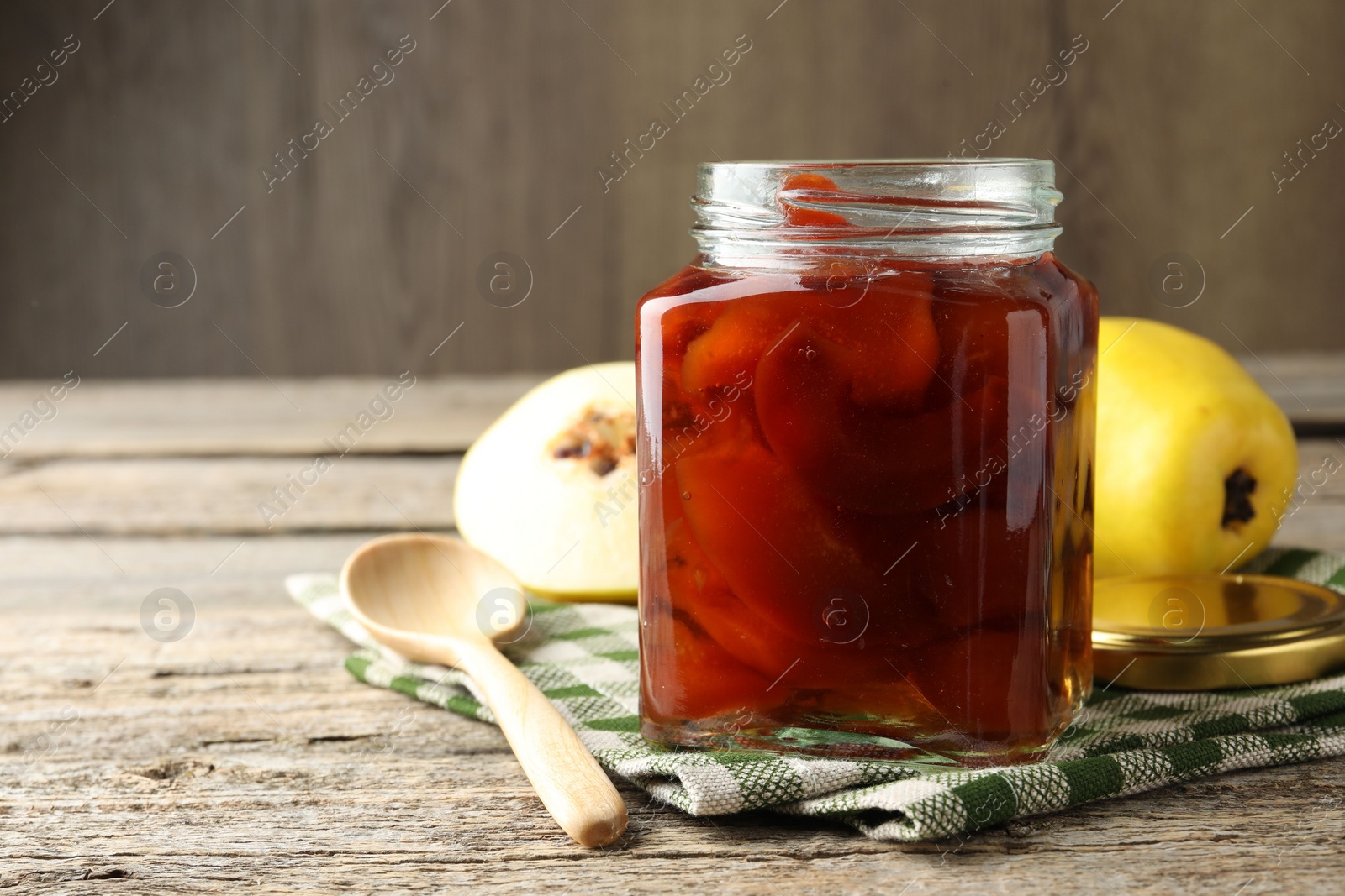 Photo of Tasty homemade quince jam in jar, spoon and fruits on wooden table, closeup. Space for text